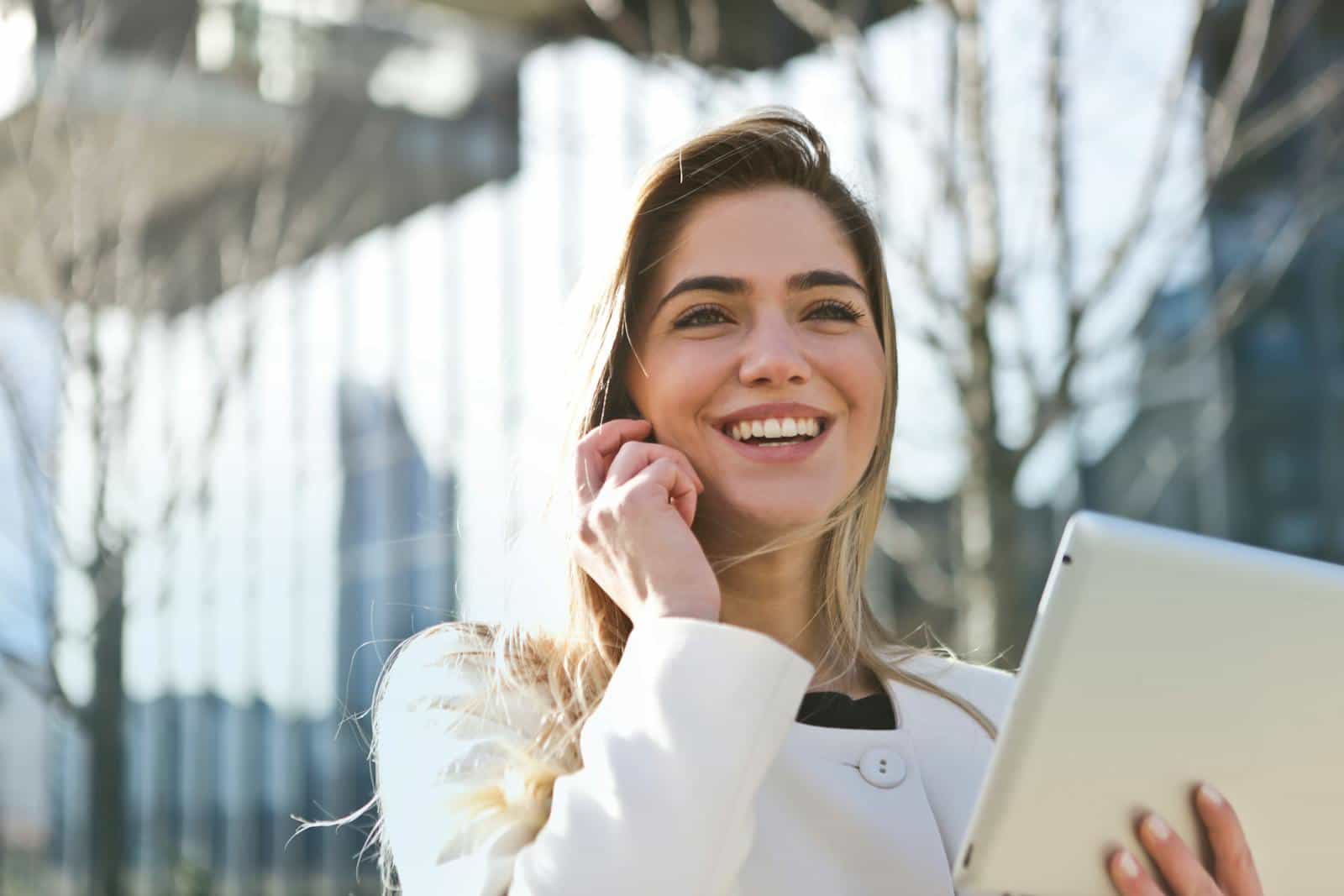 Photo by Andrea Piacquadio Confident businesswoman using her tablet and phone, smiling outdoors in sunlight.