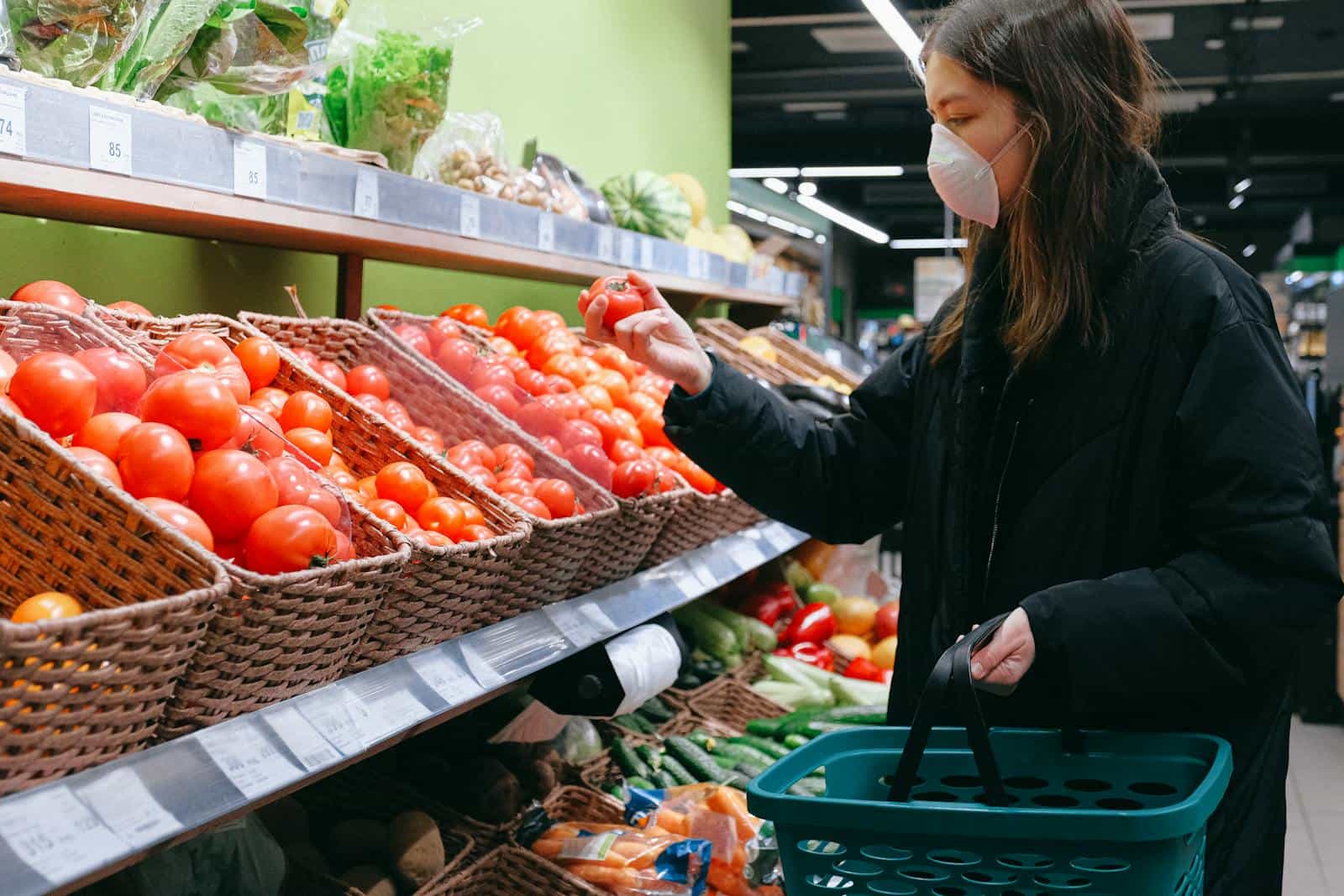 Woman in face mask selecting tomatoes at a grocery store during pandemic.