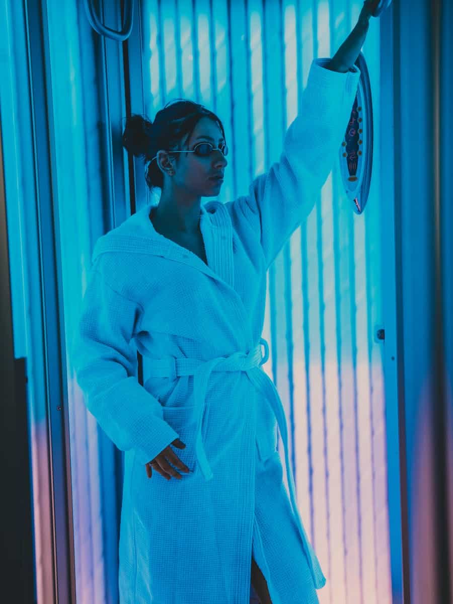 Woman in a bathrobe using a solarium indoors. Relaxing beauty treatment setting.